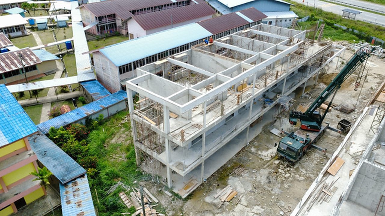 Aerial view of a three-storey reinforced concrete school block under construction with a crawler crane